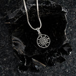 Silver necklace with a sun pendant on a dark stone surface