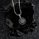 Silver necklace with a sun pendant on a dark stone surface