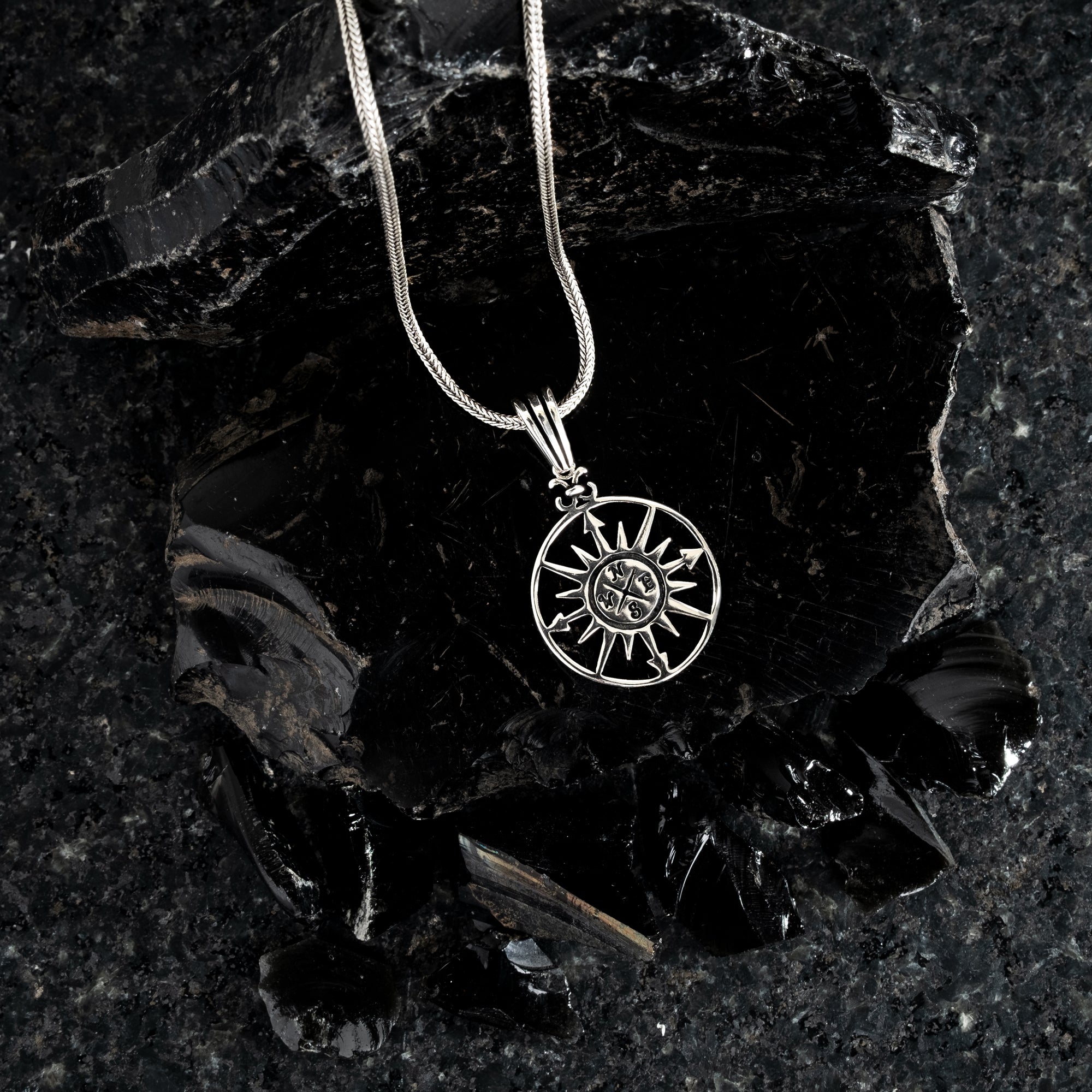 Silver necklace with a sun pendant on a dark stone surface