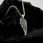 Silver leaf-shaped pendant on a chain against a dark stone background