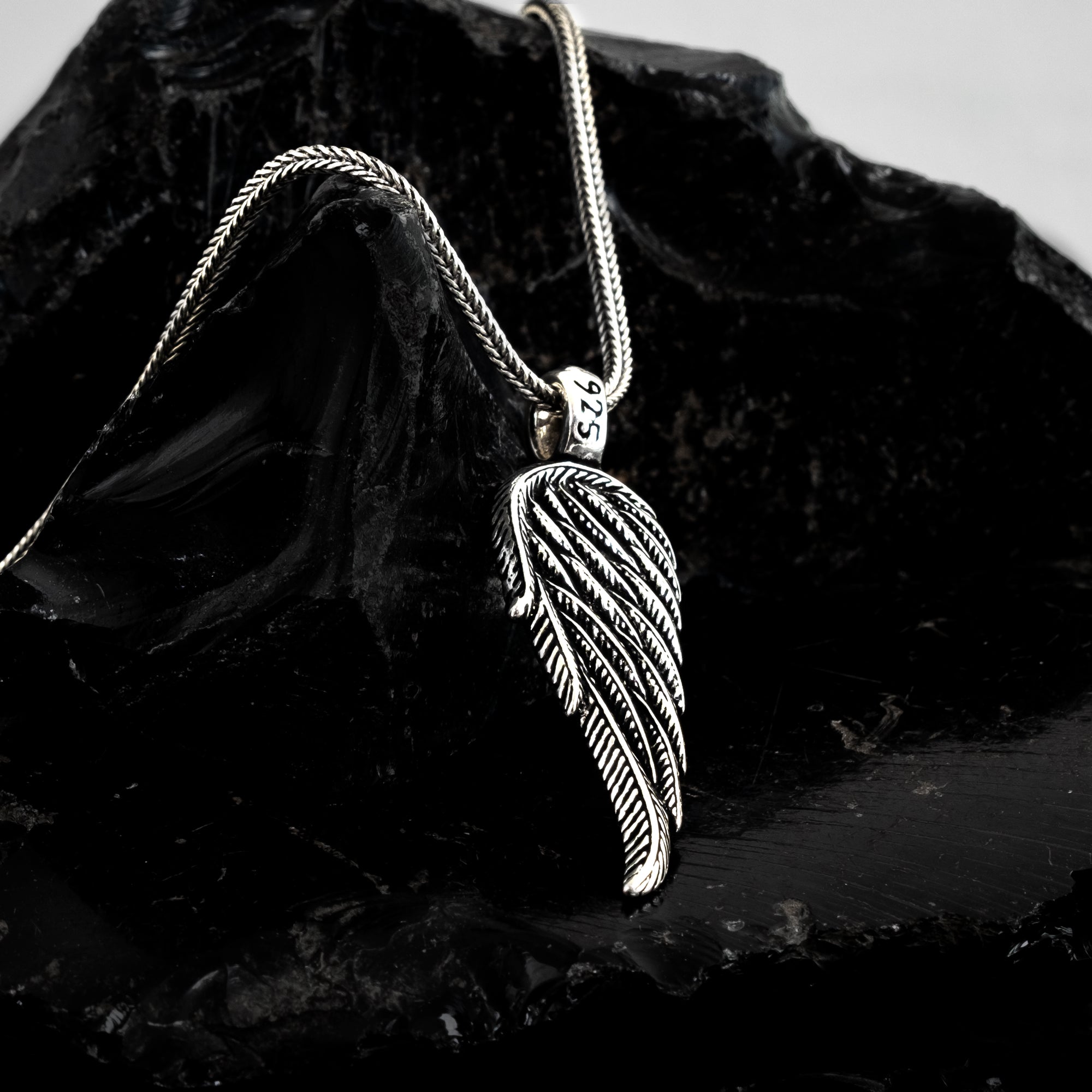 Silver leaf-shaped pendant on a chain against a dark stone background