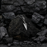 Silver pendant on a chain resting on dark, textured stones
