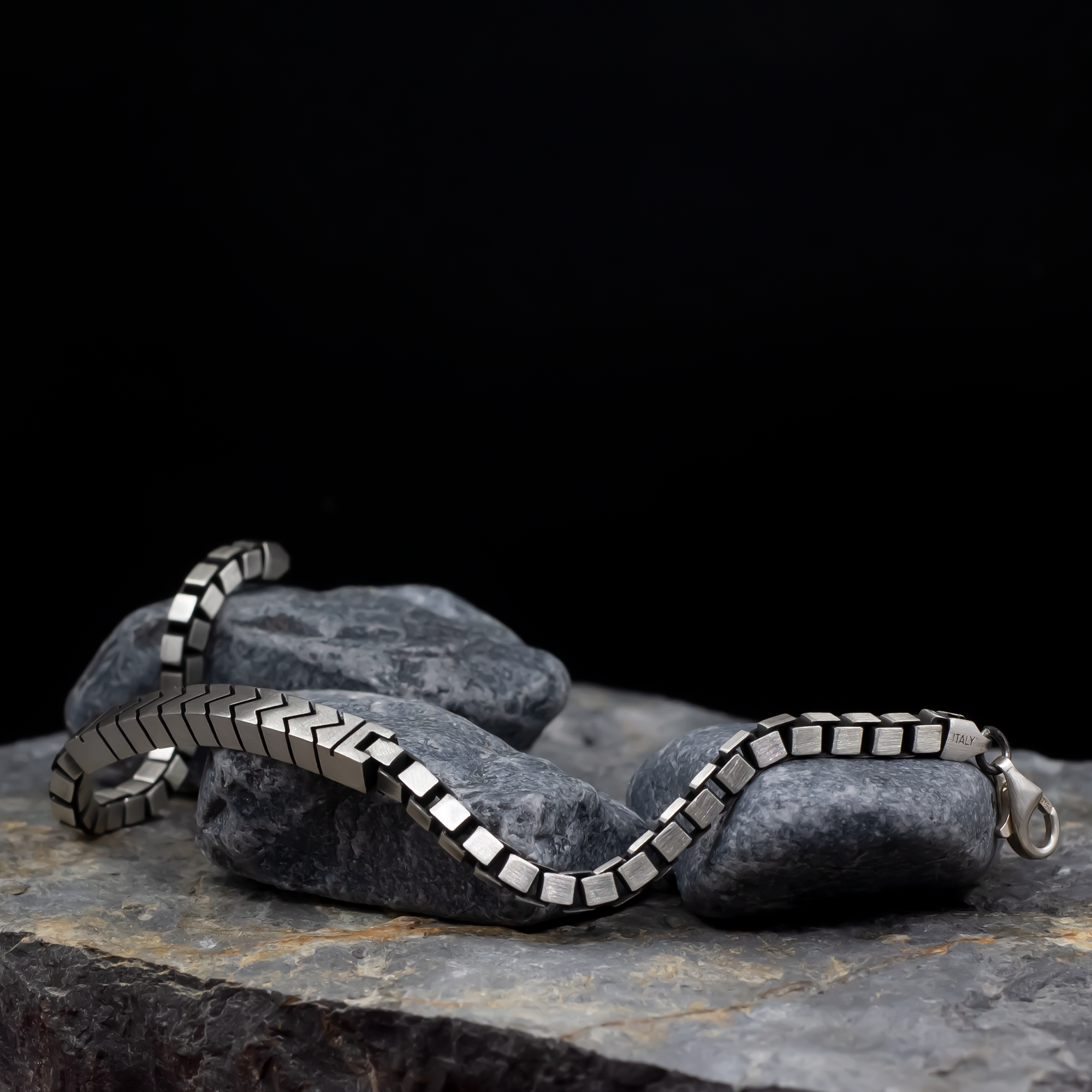Silver chain bracelet on a dark stone surface with a black background